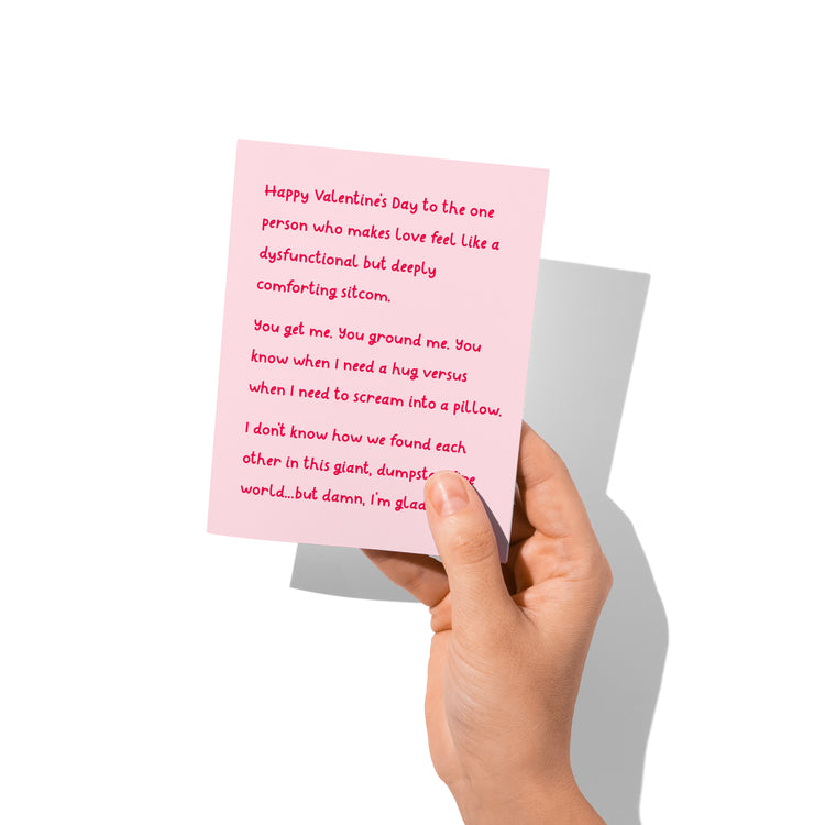 Funny Valentine’s card held in hand, humorous sitcom-style love message visible.