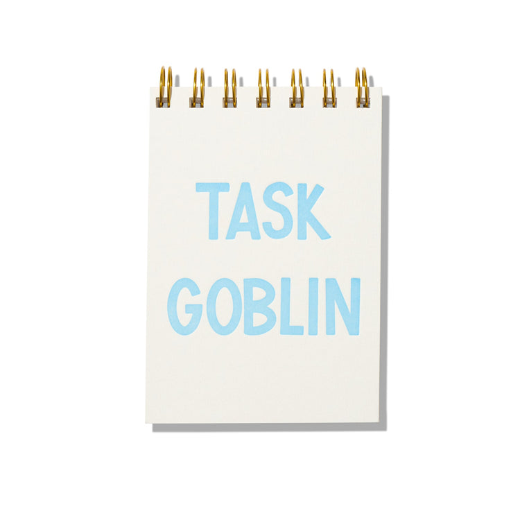 Mini jotter notebook with blue letterpress text “Task Goblin” on rigid white cover and gold spiral binding.