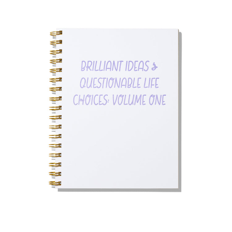 Large letterpress notebook with lavender text “Brilliant Ideas & Questionable Life Choices: Volume One” on white cover with gold spiral binding.