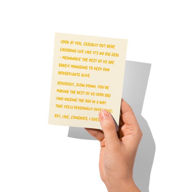 Funny congrats card held in hand, humorous overachiever message visible.