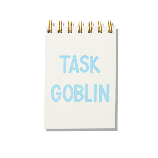 Mini jotter notebook with blue letterpress text “Task Goblin” on rigid white cover and gold spiral binding.