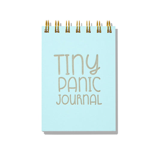Light blue letterpress mini jotter with silver text “Tiny Panic Journal” and gold spiral binding.
