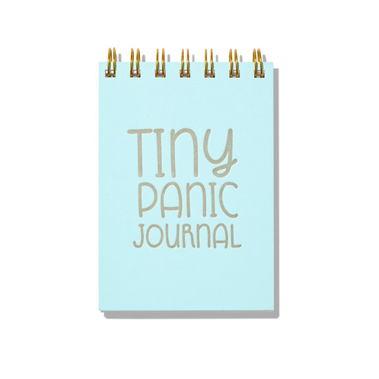 Light blue letterpress mini jotter with silver text “Tiny Panic Journal” and gold spiral binding.
