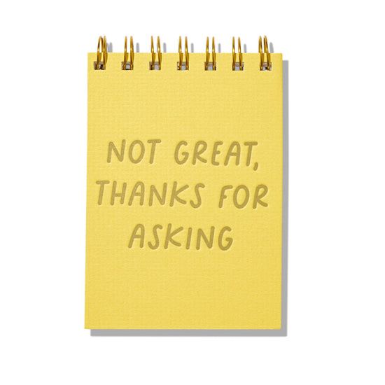 Yellow letterpress mini jotter with gold text “Not Great, Thanks for Asking” and spiral binding.
