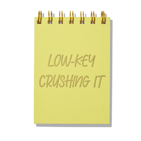 Chartreuse letterpress mini jotter with gold text “Low-Key Crushing It” and gold spiral binding.

