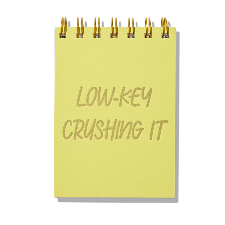 Chartreuse letterpress mini jotter with gold text “Low-Key Crushing It” and gold spiral binding.
