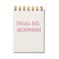 Mini jotter with pink letterpress text “Delulu, but Determined” and gold spiral binding.
