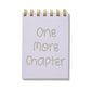 Purple mini jotter with letterpress text “One More Chapter” and gold spiral binding.