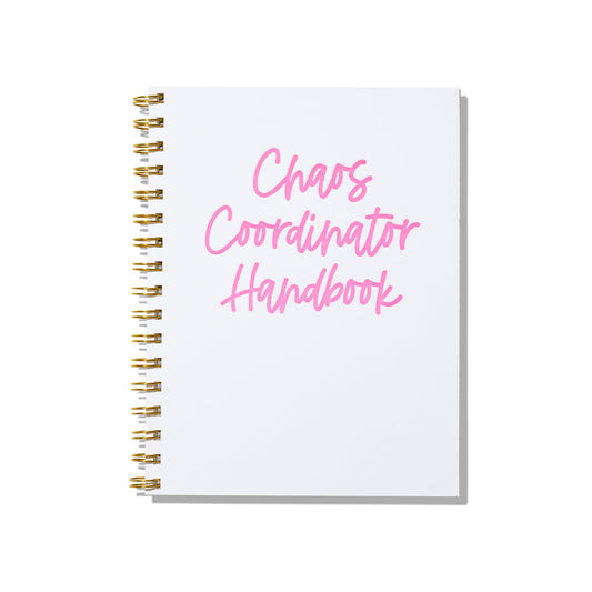Large letterpress notebook with “Chaos Coordinator Handbook” in pink text on white cover with gold spiral binding.
