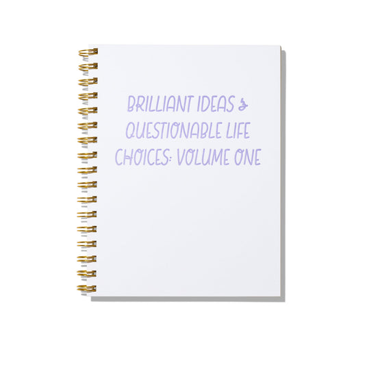 Large letterpress notebook with lavender text “Brilliant Ideas & Questionable Life Choices: Volume One” on white cover with gold spiral binding.
