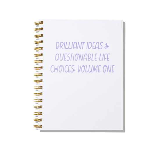 Large letterpress notebook with lavender text “Brilliant Ideas & Questionable Life Choices: Volume One” on white cover with gold spiral binding.

