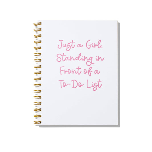 Large letterpress notebook with pink text “Just a Girl Standing in Front of a To-Do List” on white cover with gold spiral binding.
