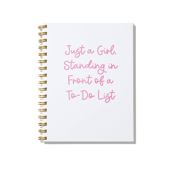 Large letterpress notebook with pink text “Just a Girl Standing in Front of a To-Do List” on white cover with gold spiral binding.

