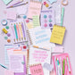 Collection of stationery items including notebooks, pens, and post-it notes on a light purple background