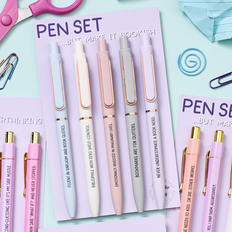 Set of pens with unique phrases on a purple card, surrounded by stationery items.